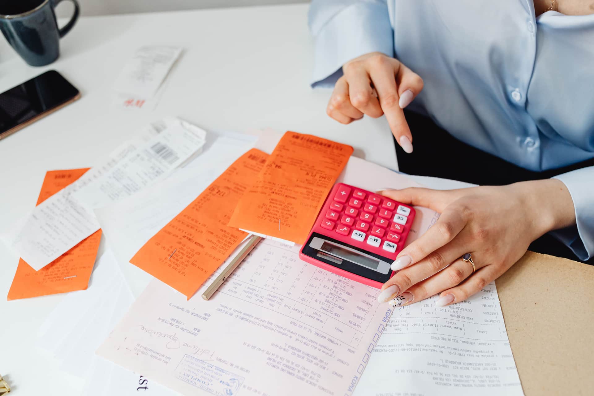 A person adding up receipts on a calculator at a desk