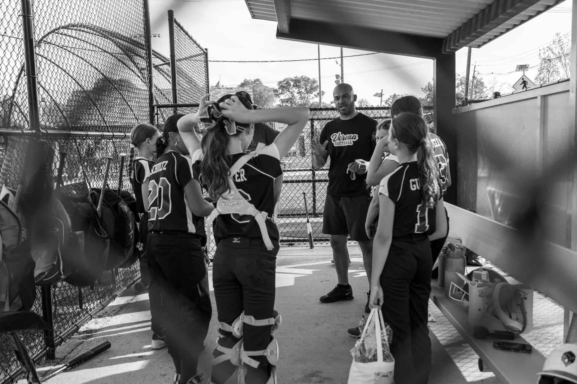 A youth softball coach talking to the team in a dugout, in black and white