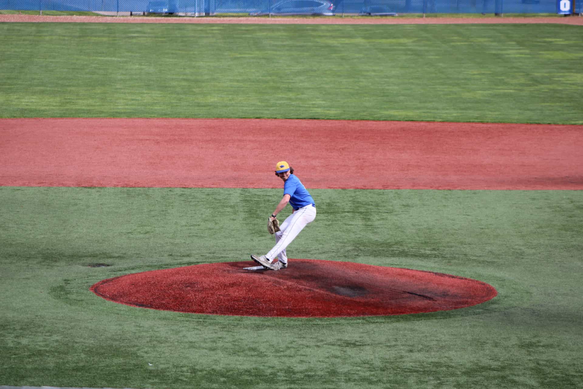 A teenage pitcher throwing from the mound on an outdoor field