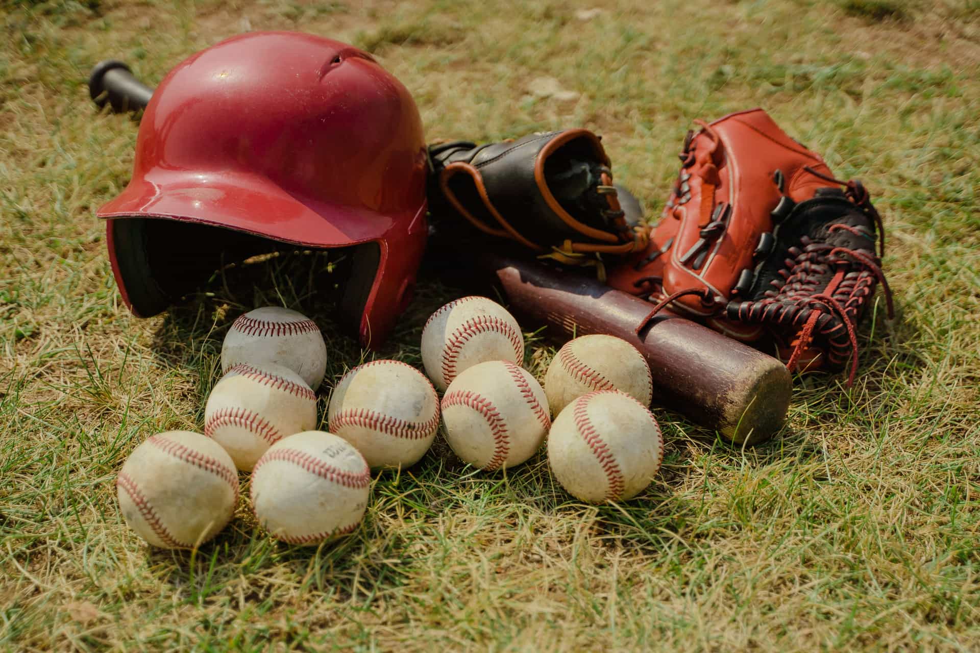 Baseball gear laid out on a grass field: balls, a bat, a batting helmet and fielding gloves