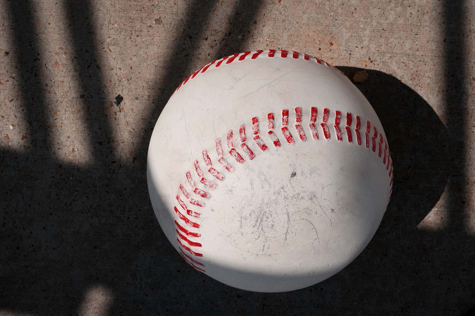 A baseball resting on a concrete surface in hard afternoon shadow