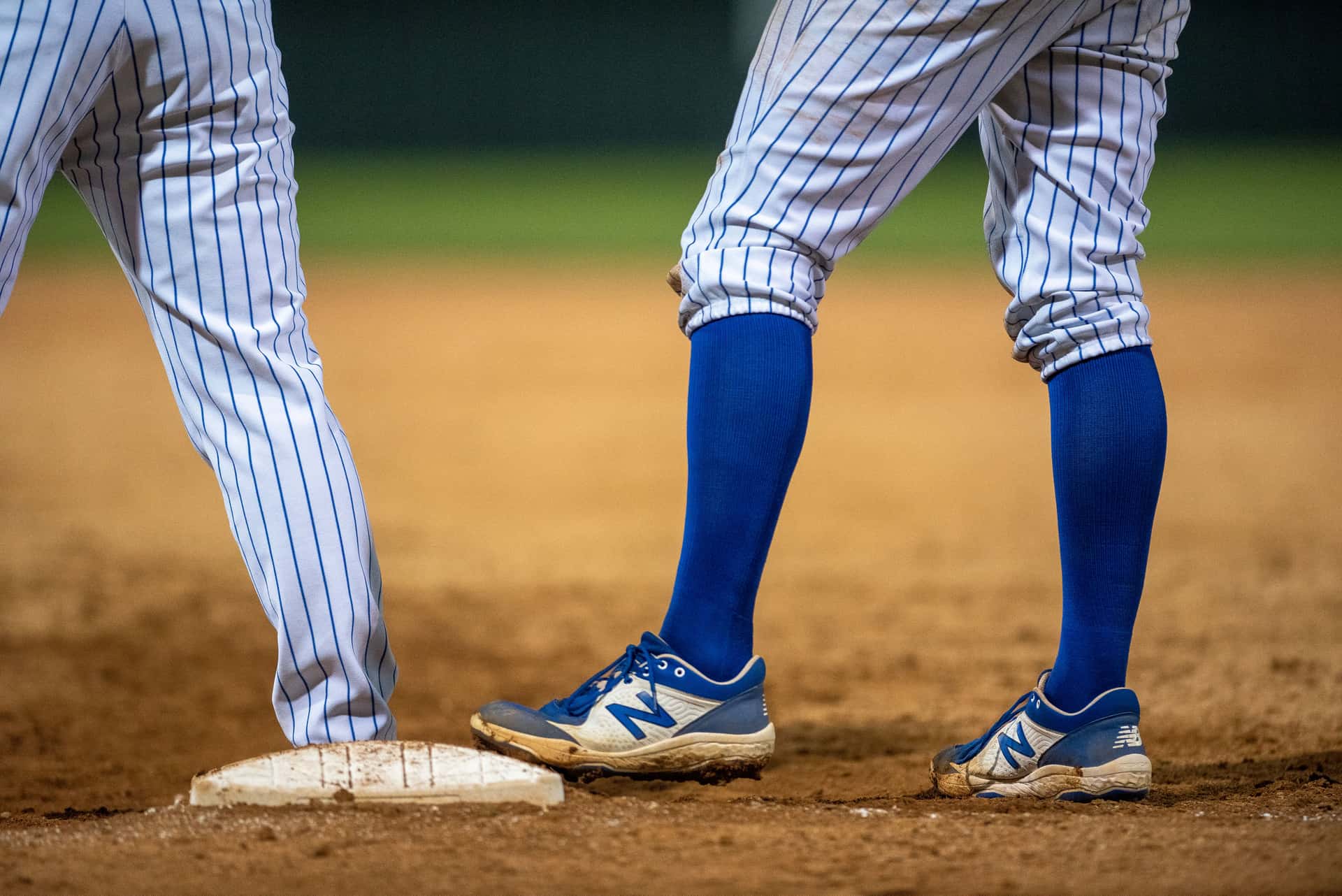 Close-up of players' cleats and blue knee socks at second base on a dirt infield