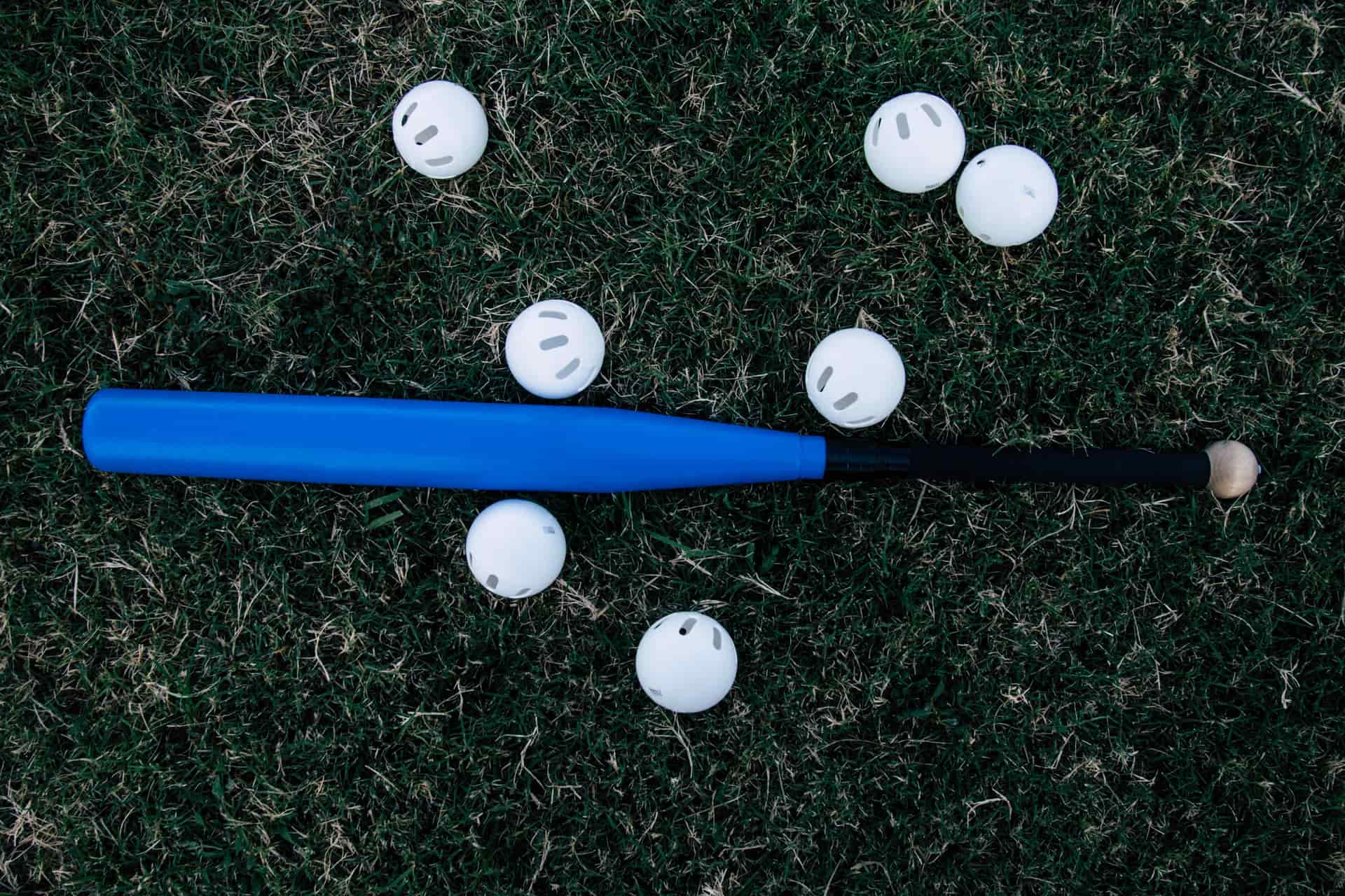 A blue aluminum bat surrounded by white practice balls on a lawn