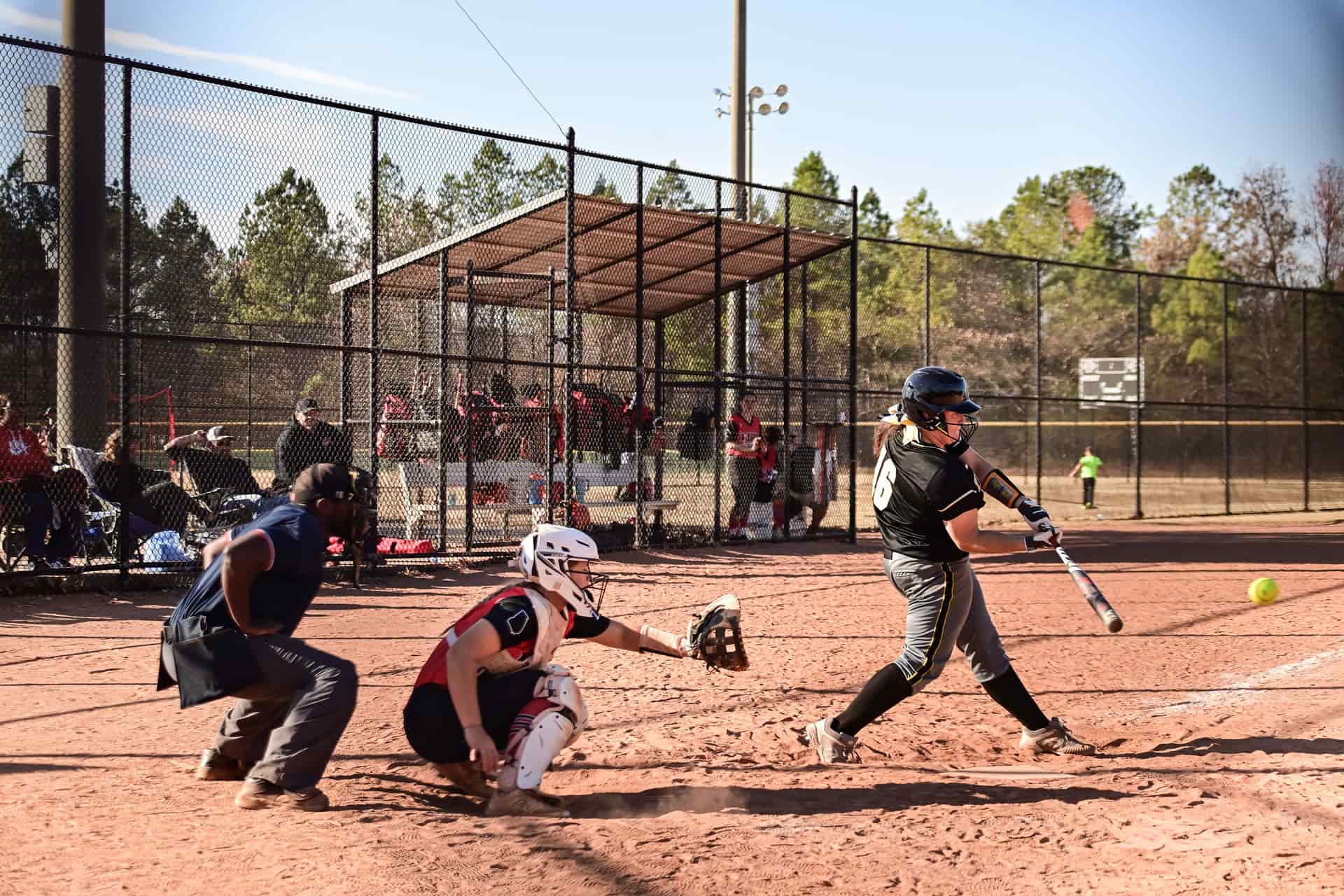 A fastpitch softball batter mid-swing on a sunny afternoon